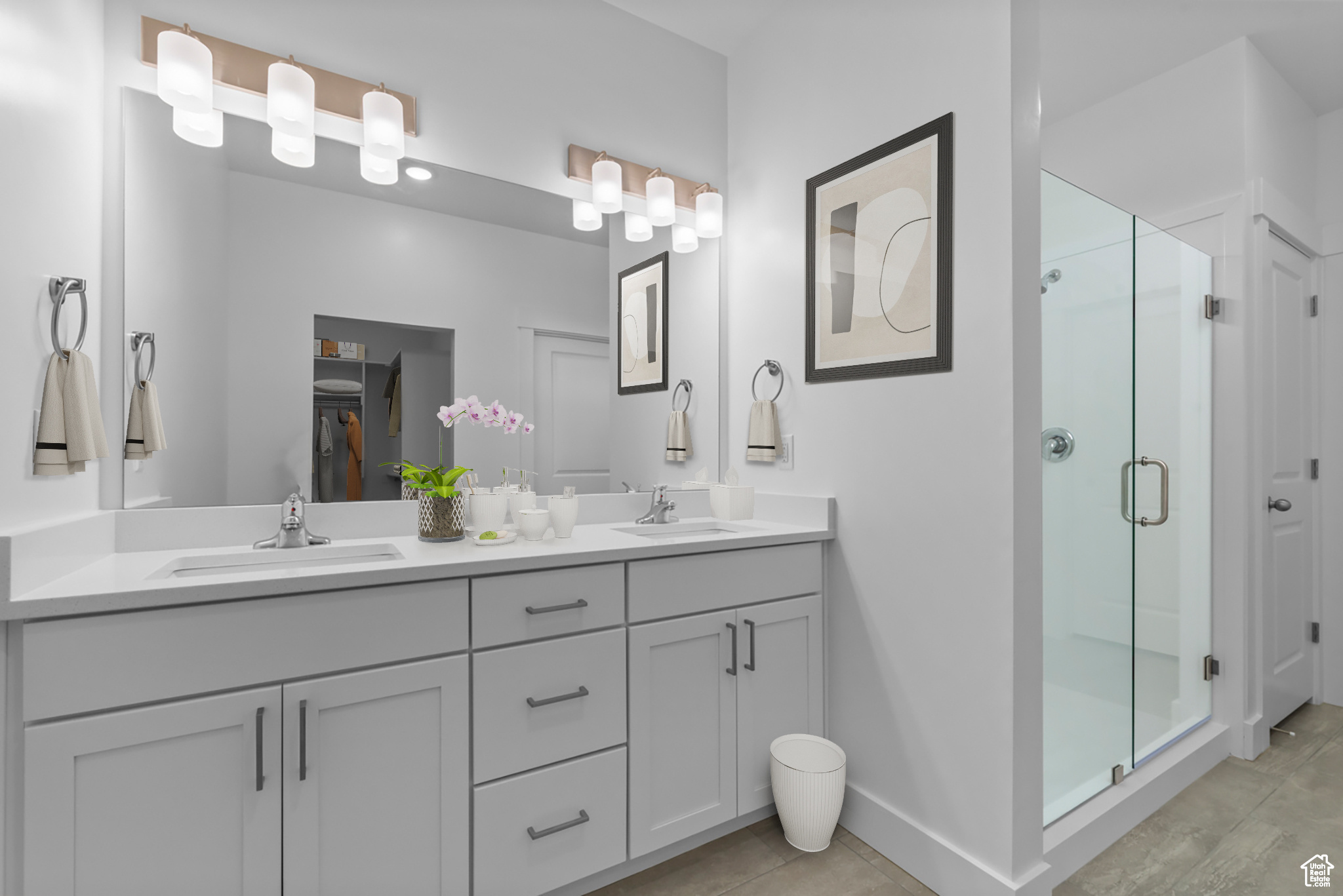 Bathroom featuring dual sinks, vanity with extensive cabinet space, and a shower with shower door