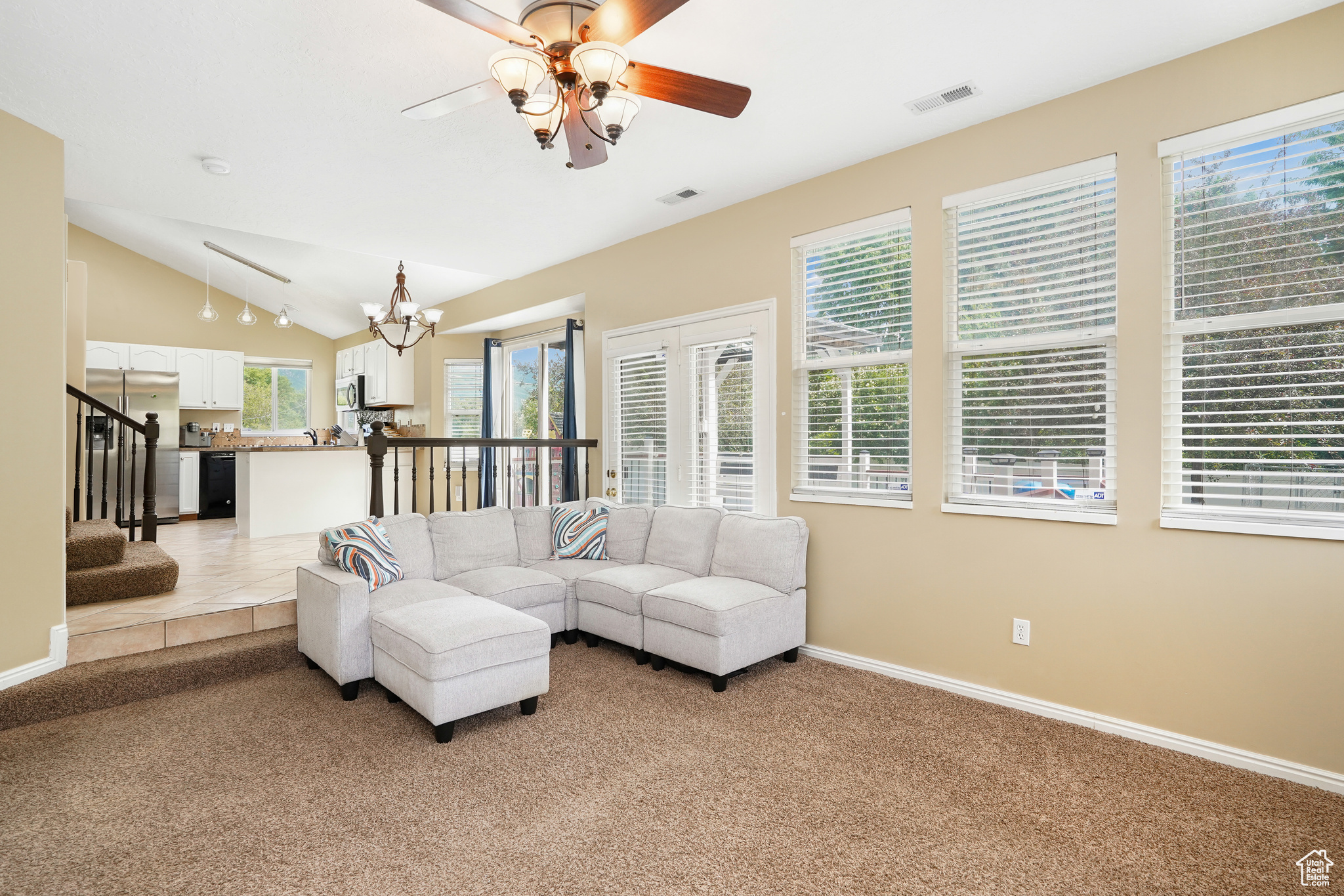 Living room featuring ceiling fan with notable chandelier, light colored carpet, and lofted ceiling