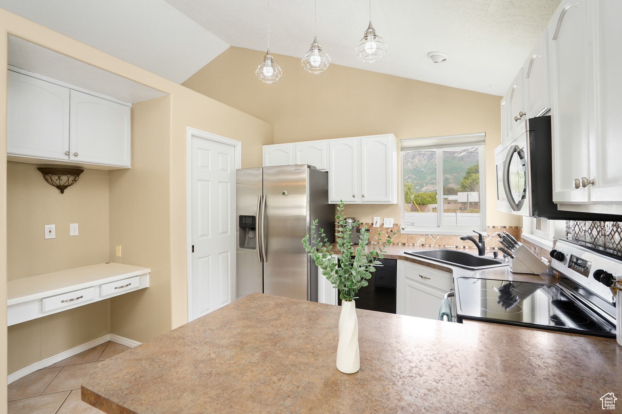 Kitchen featuring vaulted ceiling, white cabinets, and appliances with stainless steel finishes