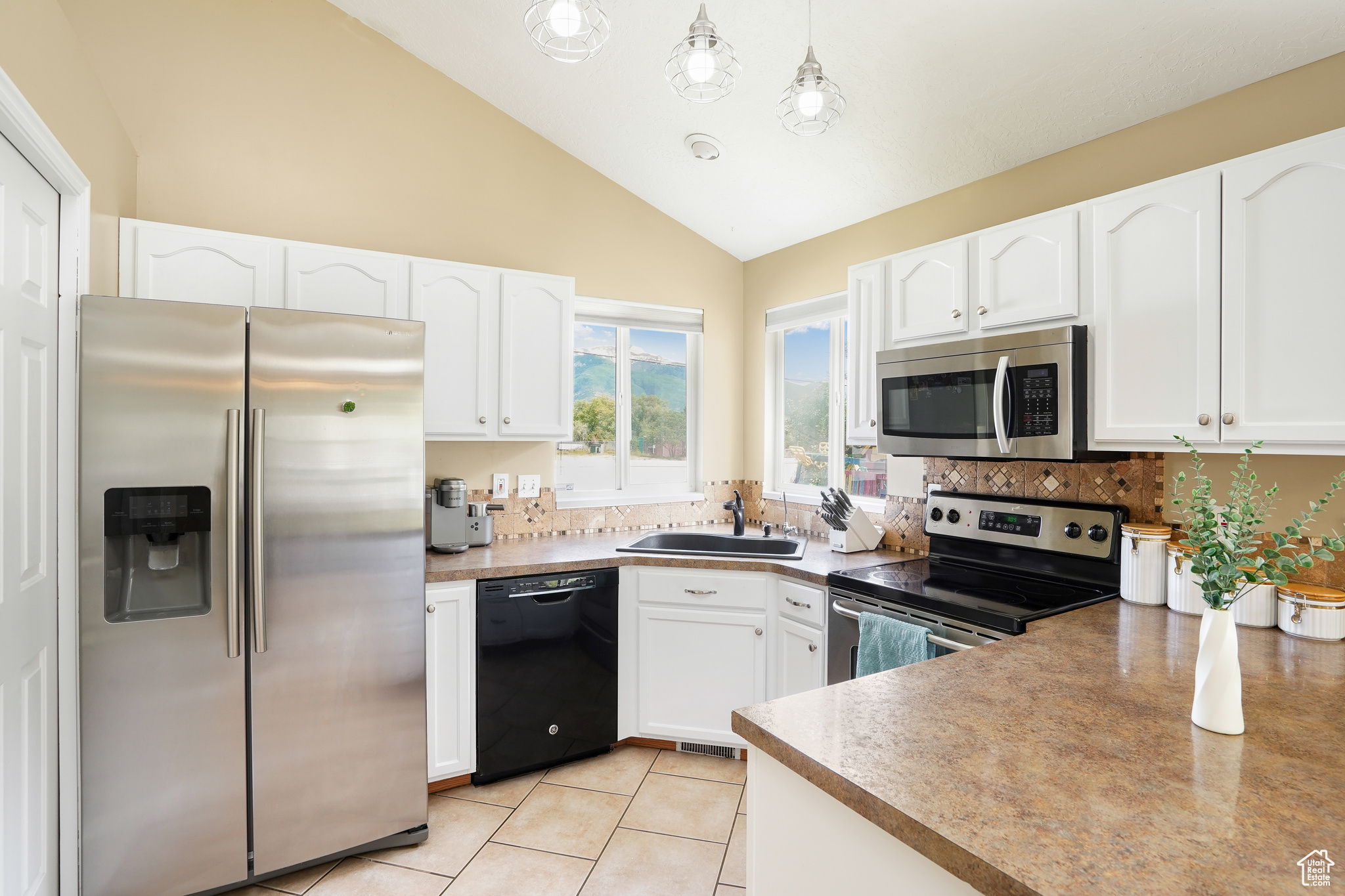 Kitchen featuring stainless steel appliances, light tile floors, hanging light fixtures, lofted ceiling, and white cabinetry