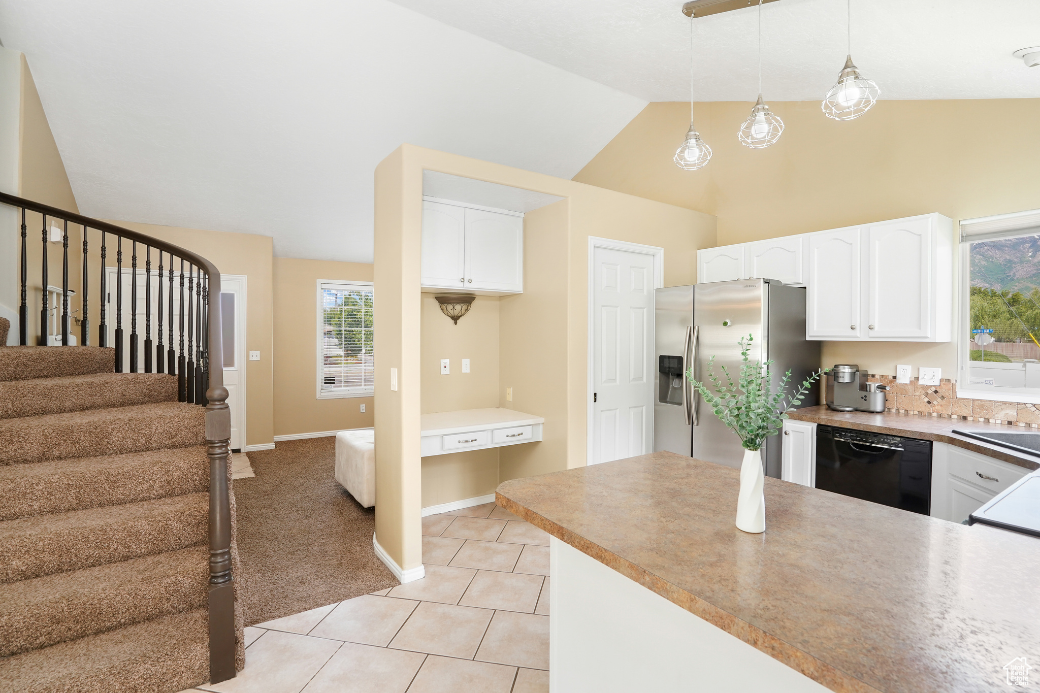 Kitchen featuring decorative light fixtures, vaulted ceiling, stainless steel fridge with ice dispenser, black dishwasher, and white cabinetry