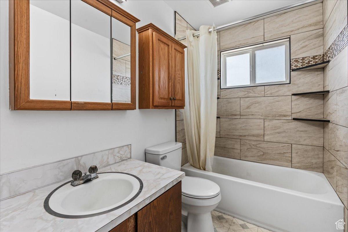 Full bathroom with tile flooring, toilet, vanity, and shower / bath combo