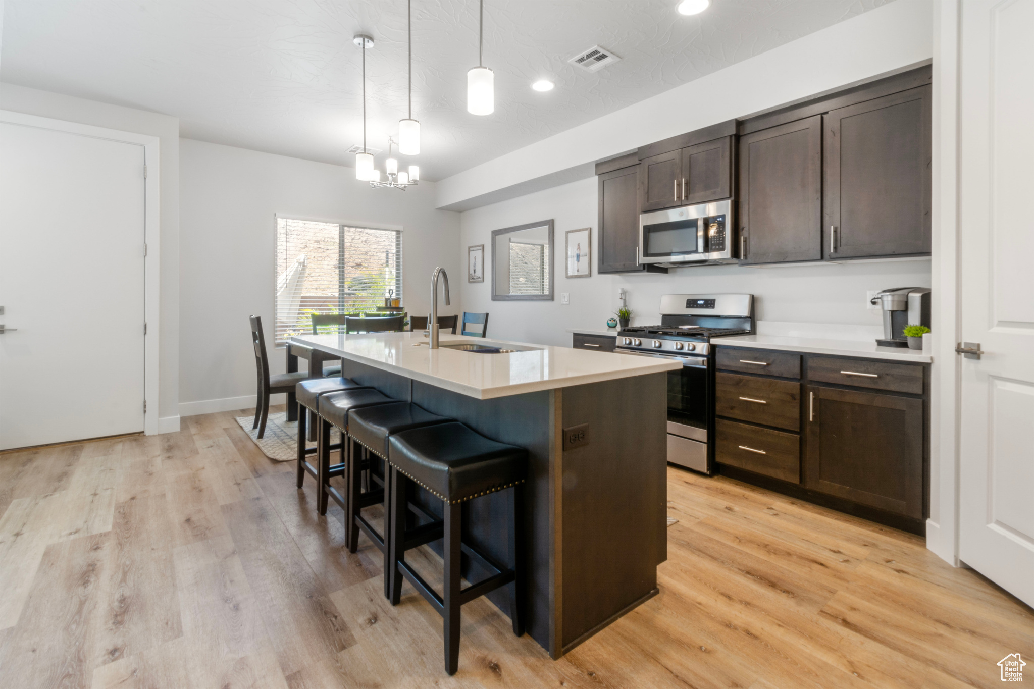 Kitchen featuring light wood-type flooring, hanging light fixtures, sink, a kitchen island with sink, and appliances with stainless steel finishes