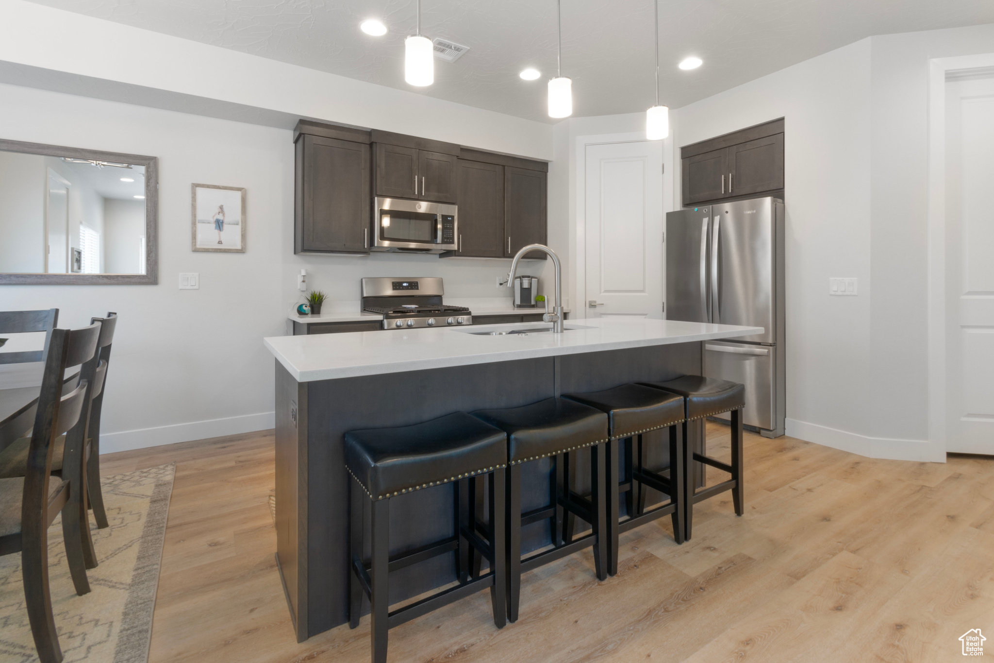 Kitchen featuring light hardwood / wood-style flooring, stainless steel appliances, dark brown cabinets, sink, and pendant lighting