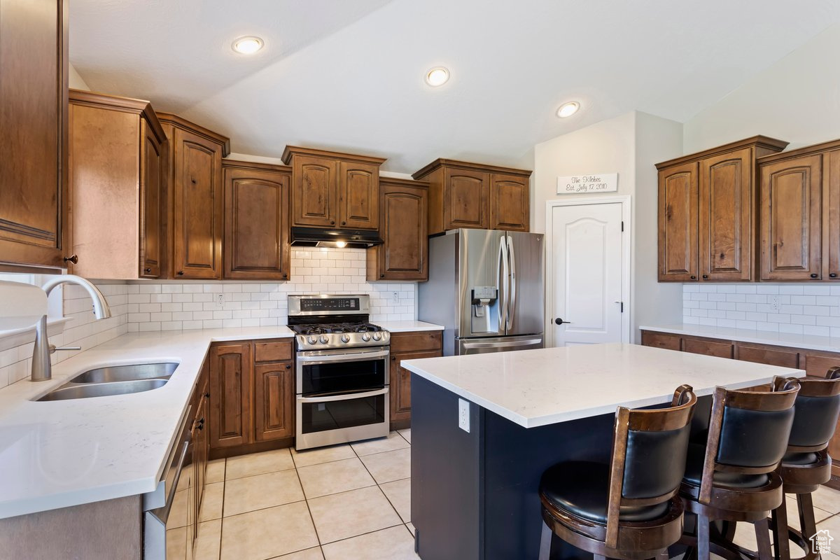 Kitchen featuring stainless steel appliances, vaulted ceiling, backsplash, a center island, and sink