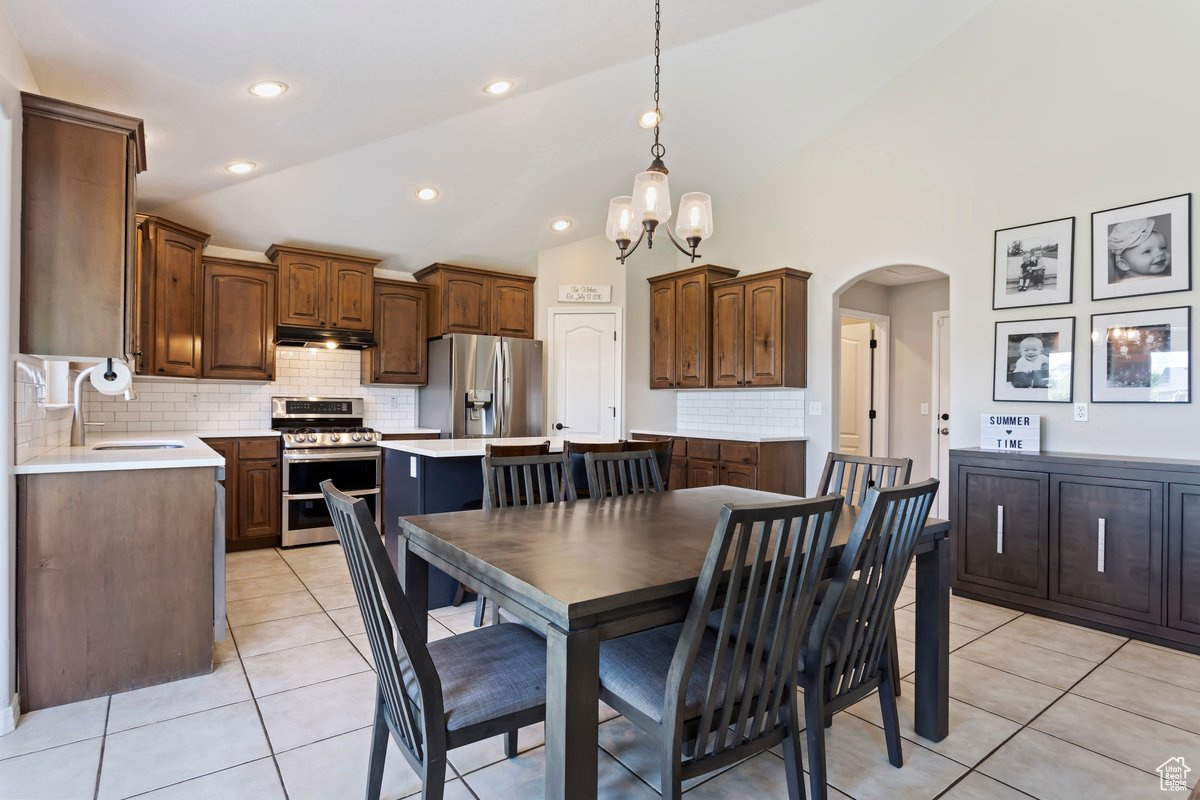 Dining area with high vaulted ceiling, sink, light tile flooring, and an inviting chandelier