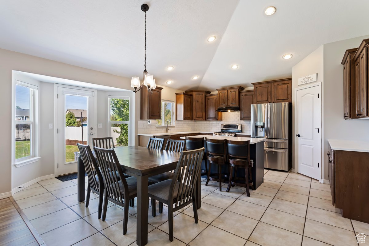 Tiled dining area featuring a notable chandelier, sink, lofted ceiling, and plenty of natural light