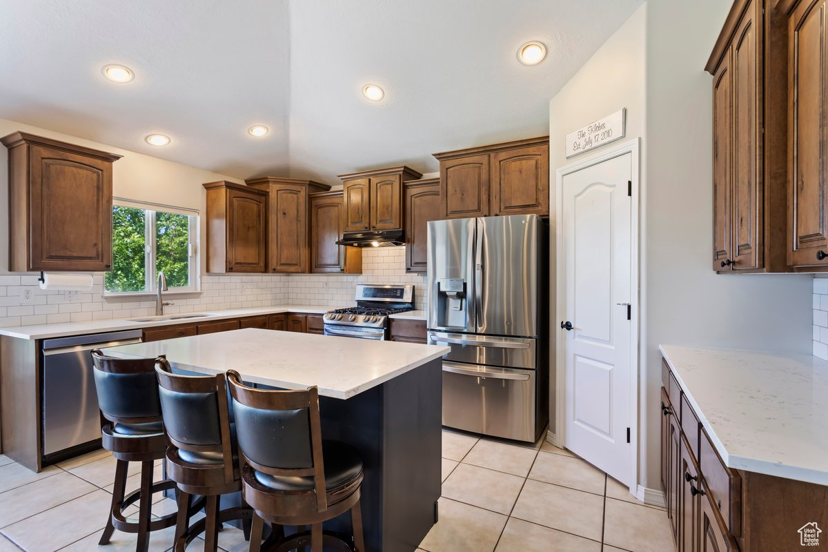 Kitchen with backsplash, appliances with stainless steel finishes, sink, and light tile floors