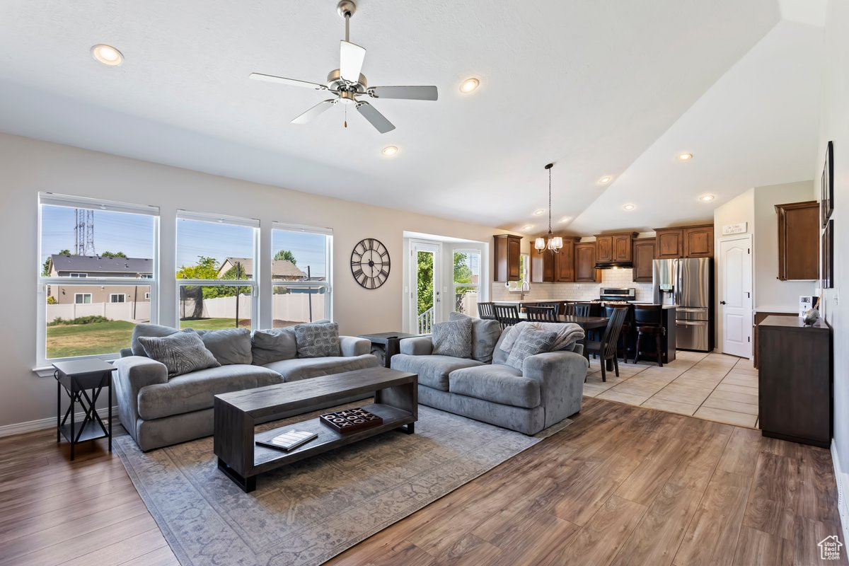 Living room featuring high vaulted ceiling, light hardwood / wood-style flooring, and ceiling fan with notable chandelier