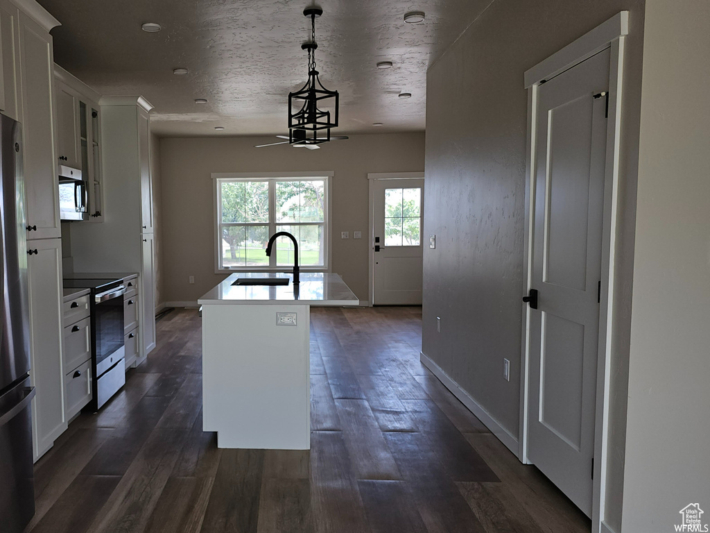 Kitchen featuring dark hardwood / wood-style flooring, stainless steel appliances, hanging light fixtures, an island with sink, and sink