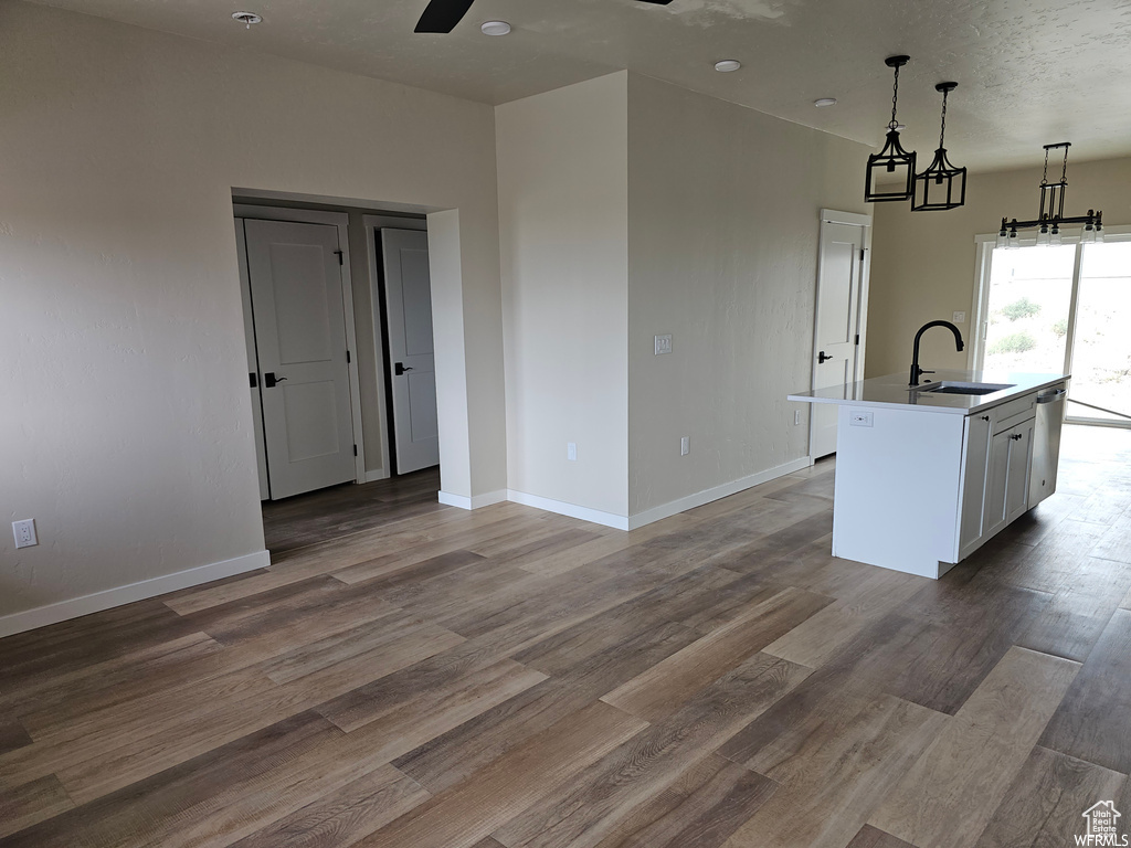 Kitchen featuring hanging light fixtures, white cabinets, hardwood / wood-style flooring, a kitchen island with sink, and sink