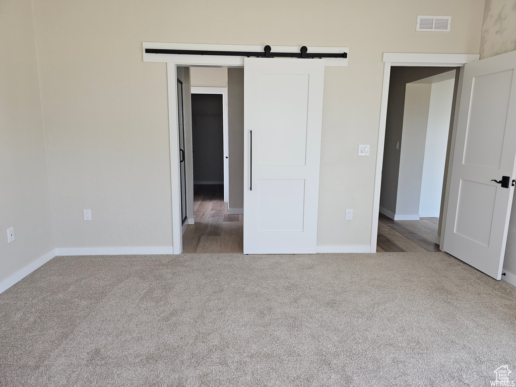 Unfurnished bedroom featuring a barn door and dark hardwood / wood-style flooring