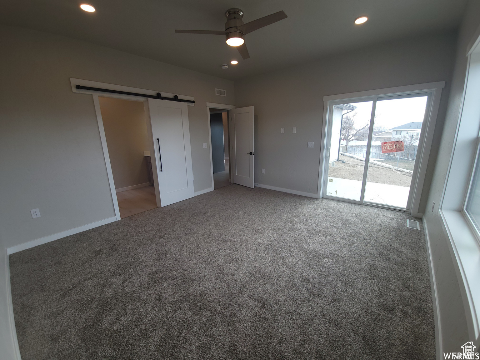 Unfurnished bedroom featuring carpet, ceiling fan, a barn door, and access to outside