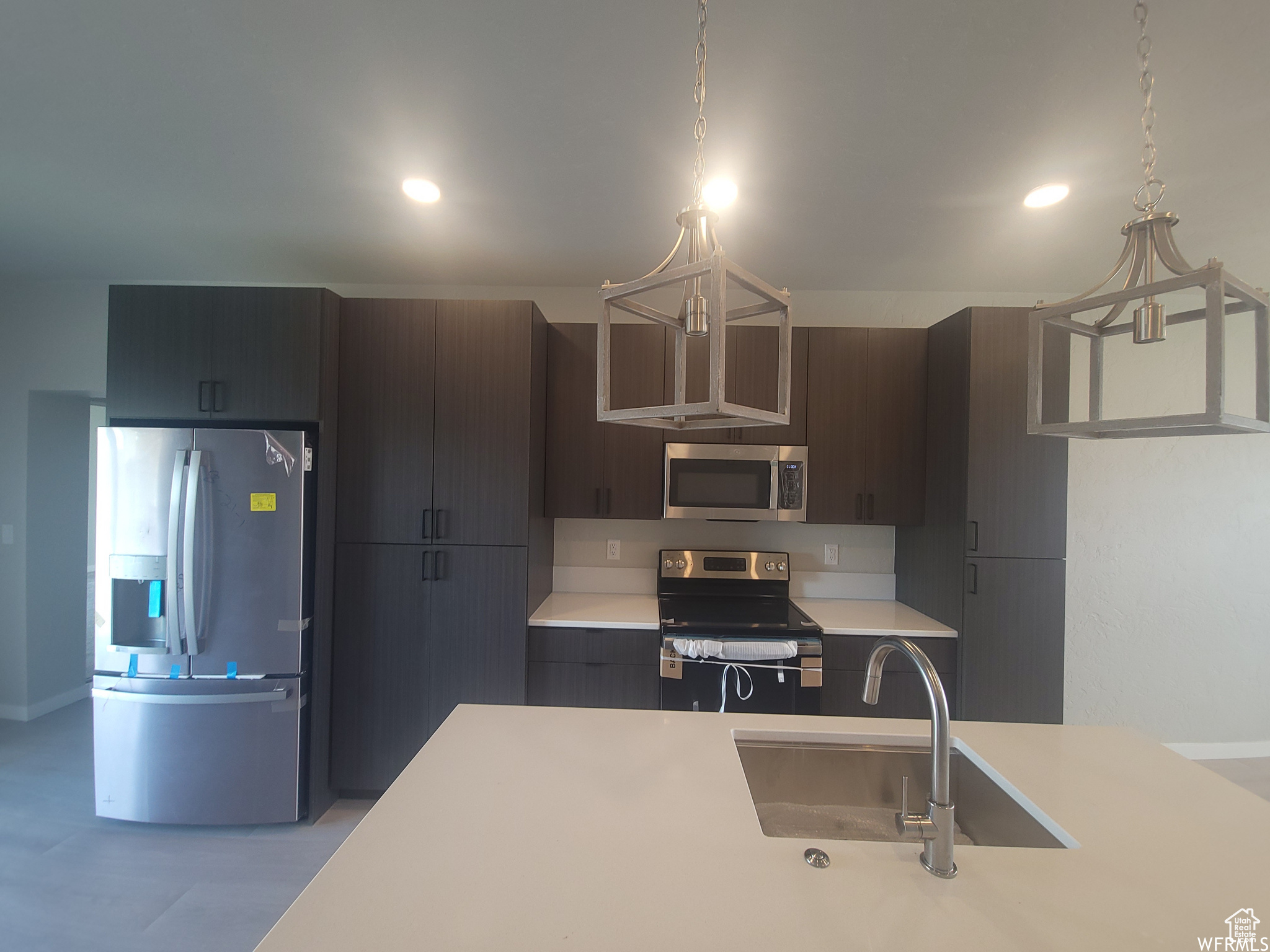 Kitchen featuring stainless steel appliances, hanging light fixtures, sink, and dark brown cabinetry