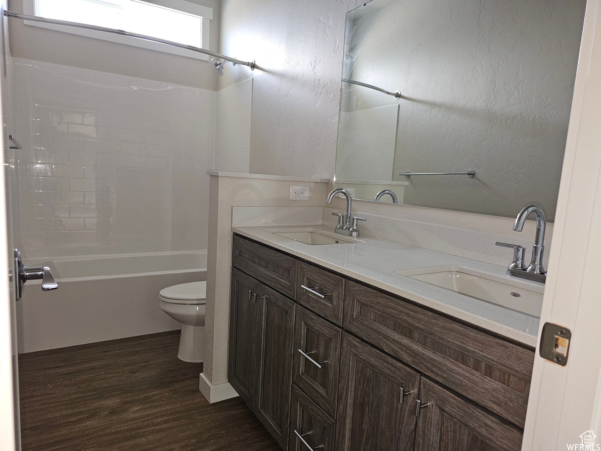 Full bathroom with dual sinks, hardwood / wood-style floors, washtub / shower combination, toilet, and large vanity