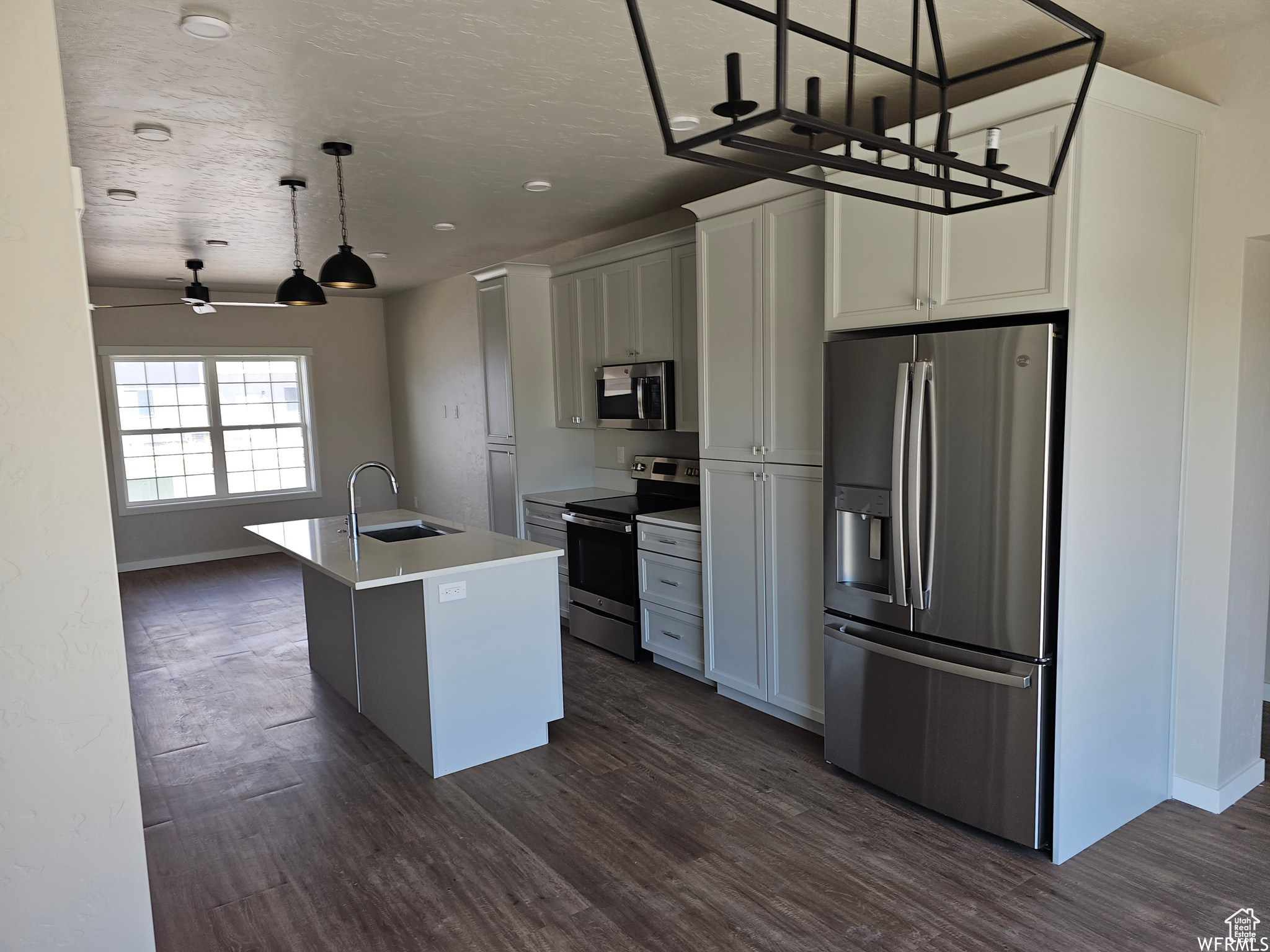 Kitchen featuring stainless steel appliances, decorative light fixtures, dark hardwood / wood-style flooring, and a kitchen island with sink