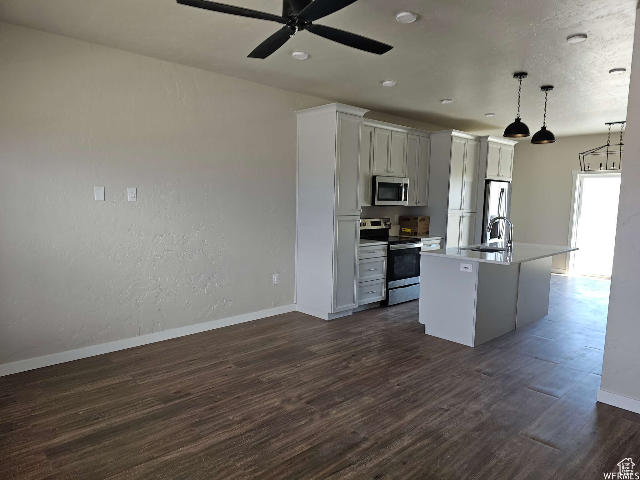 Kitchen featuring hanging light fixtures, dark hardwood / wood-style floors, a center island with sink, and stainless steel appliances