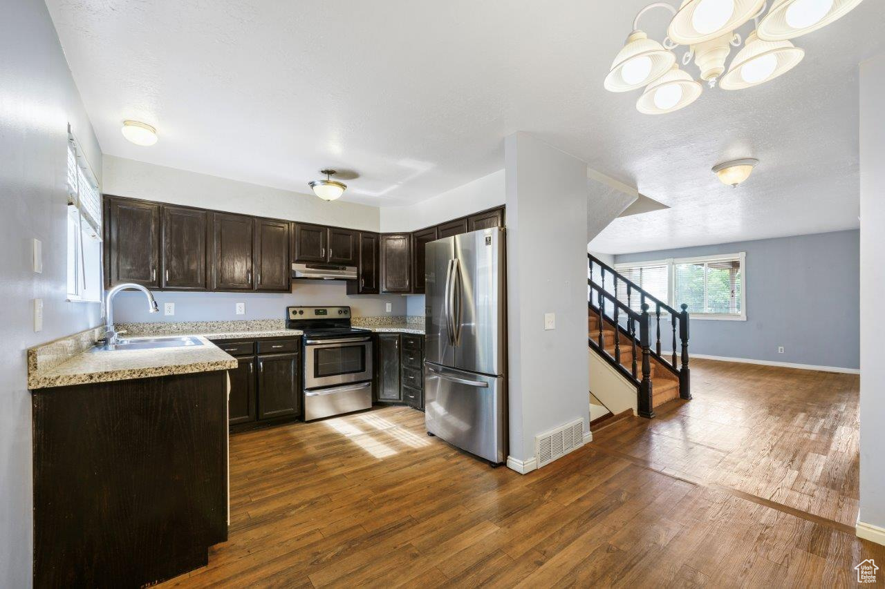 Kitchen featuring dark wood-type flooring, appliances with stainless steel finishes, light stone counters, a notable chandelier, and sink