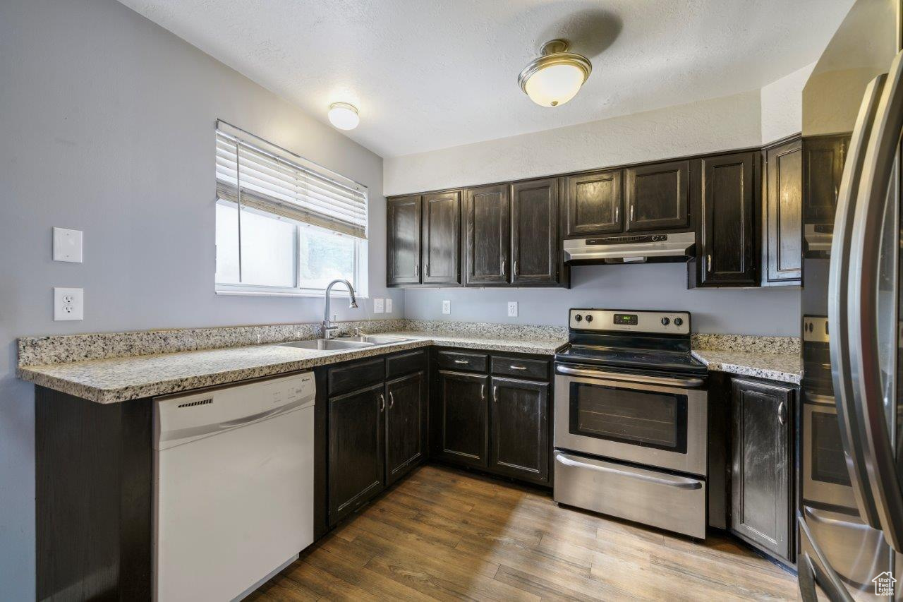 Kitchen featuring dark brown cabinetry, sink, wood-type flooring, and appliances with stainless steel finishes