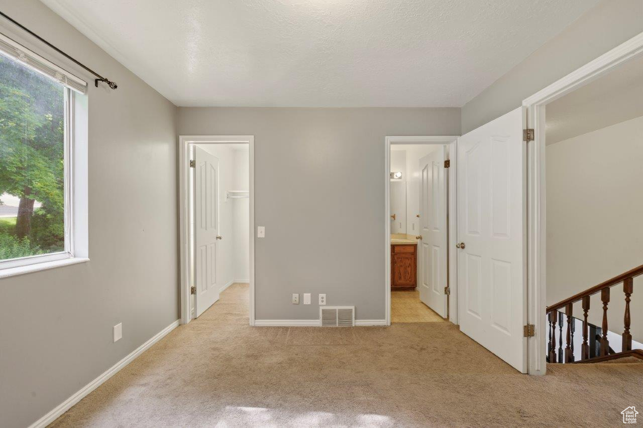 Bedroom featuring light carpet, a spacious closet, multiple windows, and ensuite bath