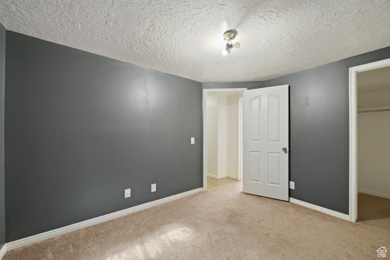 Bedroom featuring a closet, a walk in closet, a textured ceiling, and light carpet