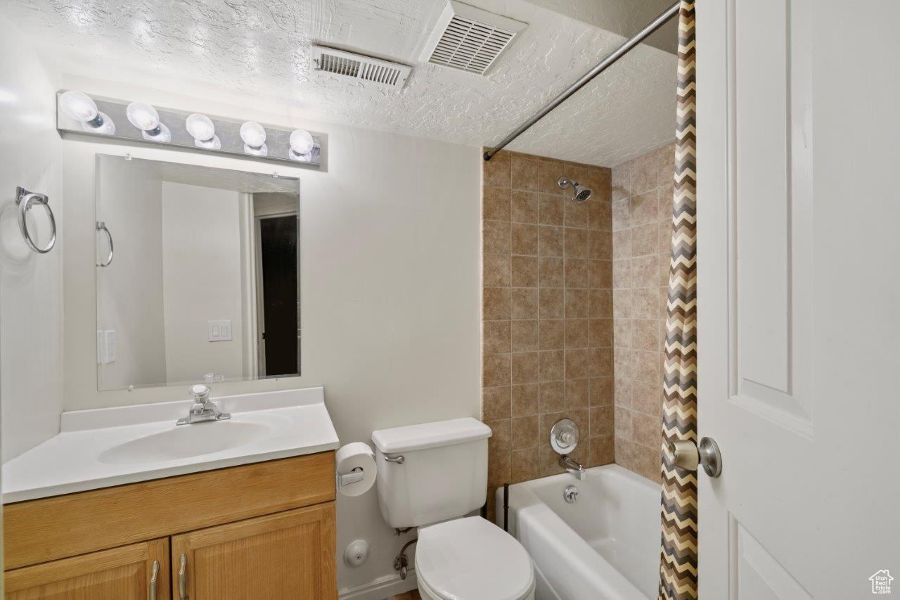 Full bathroom with a textured ceiling, vanity, toilet, and tiled shower / bath combo