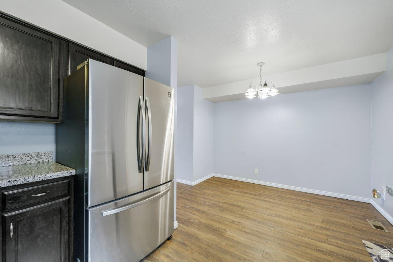 Kitchen featuring light hardwood / wood-style floors, light stone countertops, stainless steel fridge, and a notable chandelier