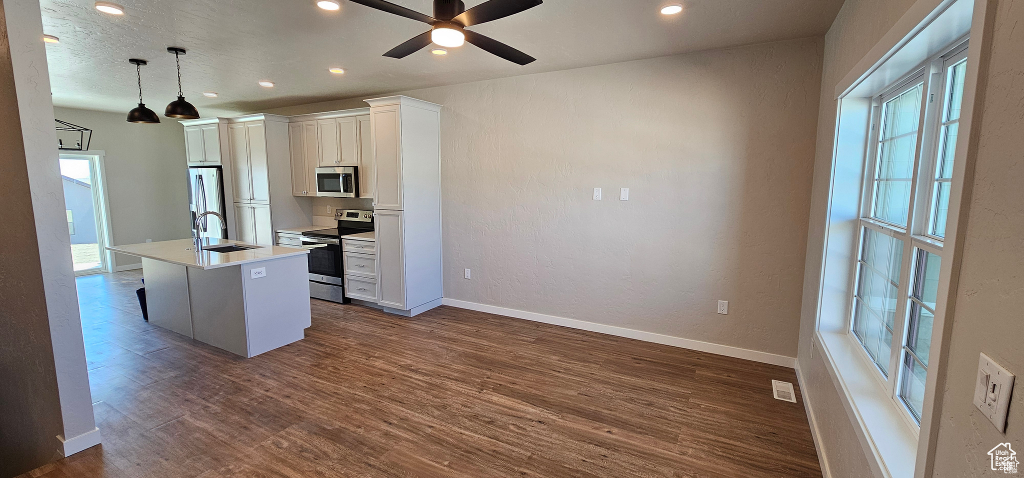 Kitchen featuring stainless steel appliances, dark wood-type flooring, a center island with sink, and white cabinets