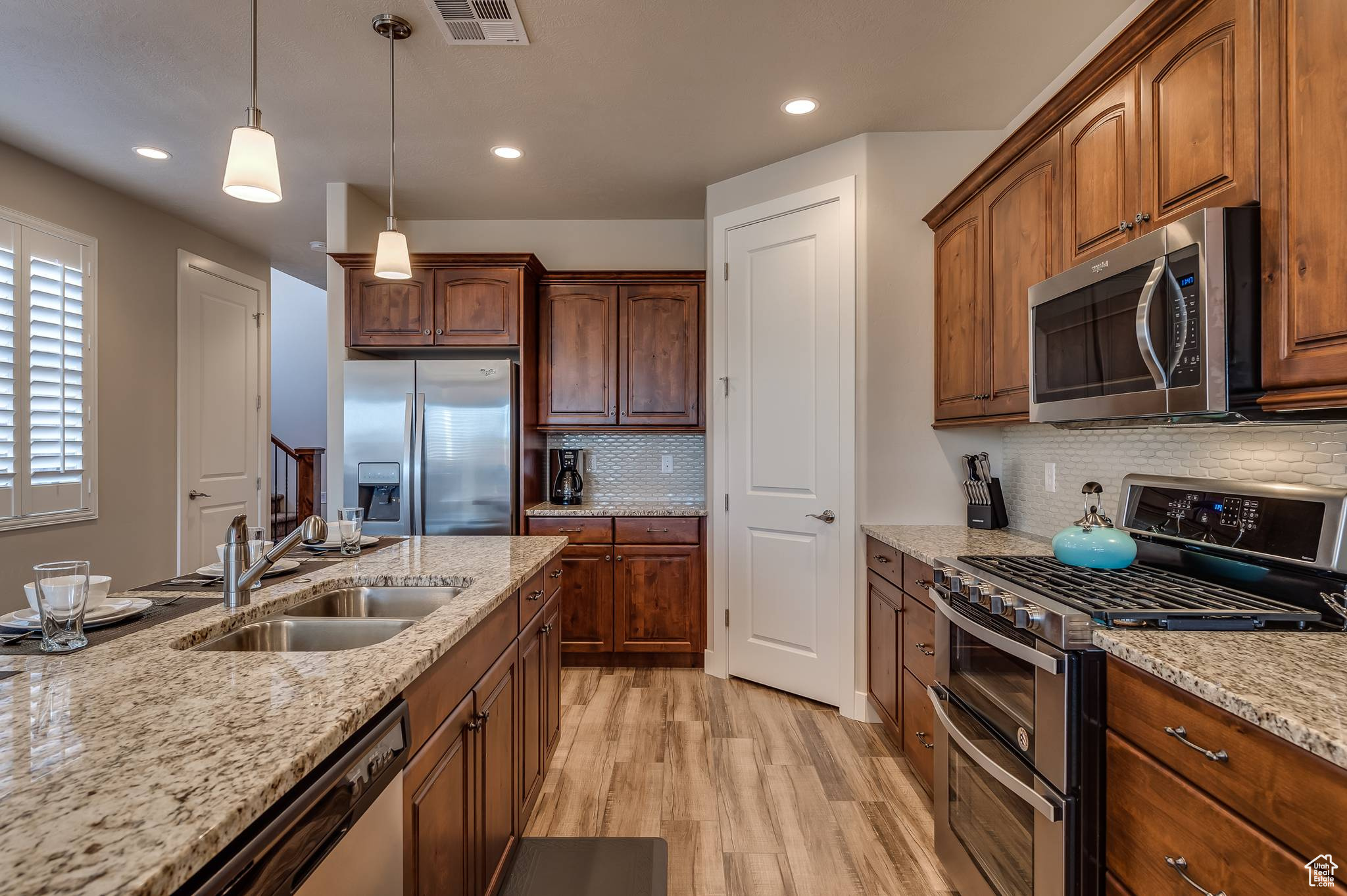 Kitchen with stainless steel appliances, backsplash, light stone countertops, light wood-type flooring, and sink