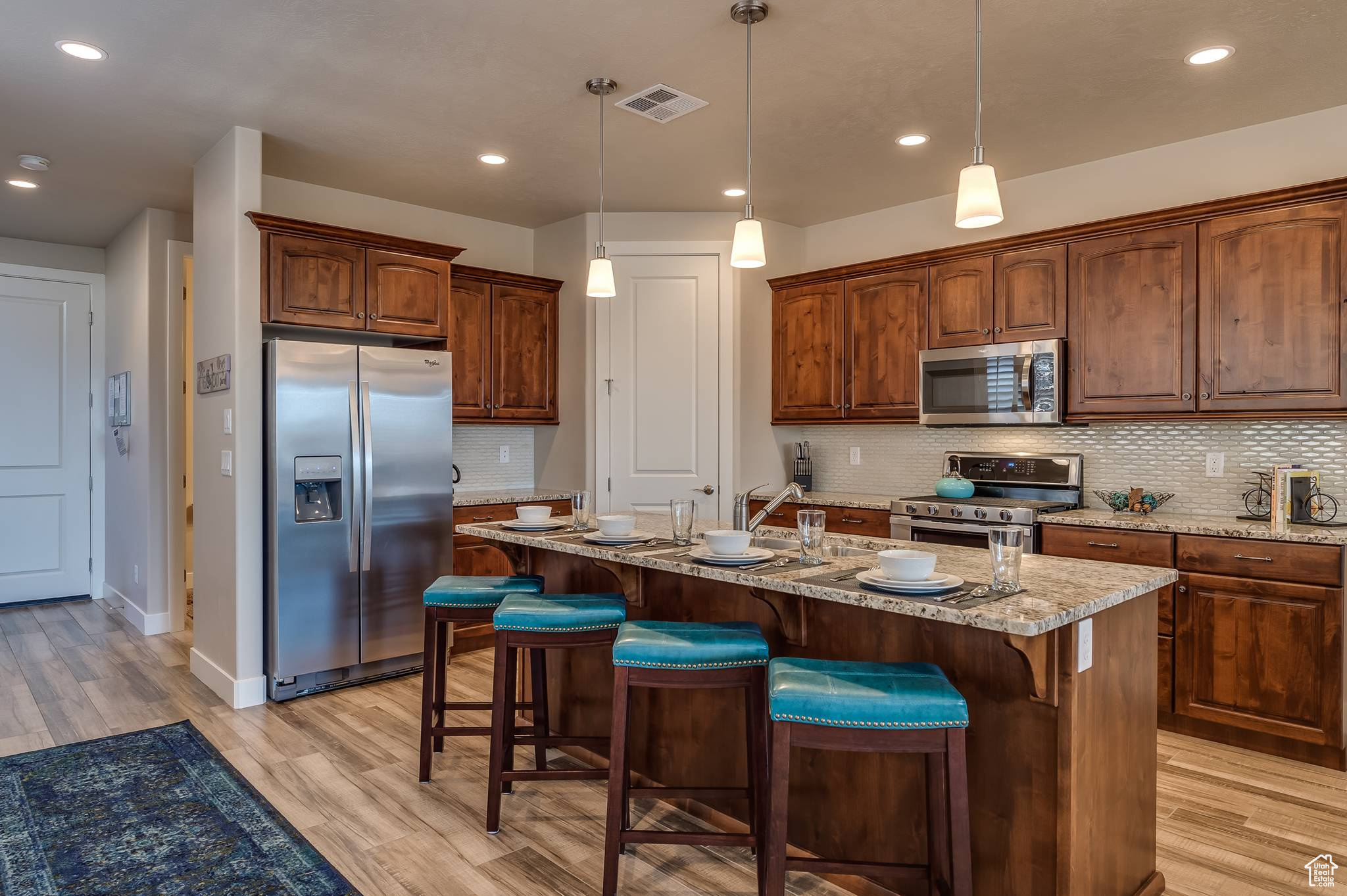 Kitchen featuring a kitchen island with sink, tasteful backsplash, light wood-type flooring, and stainless steel appliances