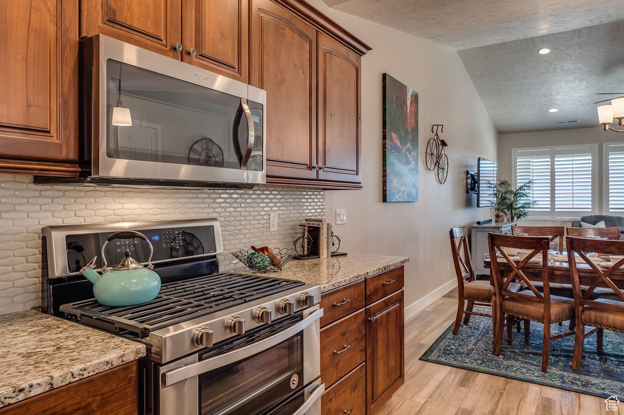 Kitchen featuring light wood-type flooring, stainless steel appliances, light stone counters, tasteful backsplash, and vaulted ceiling