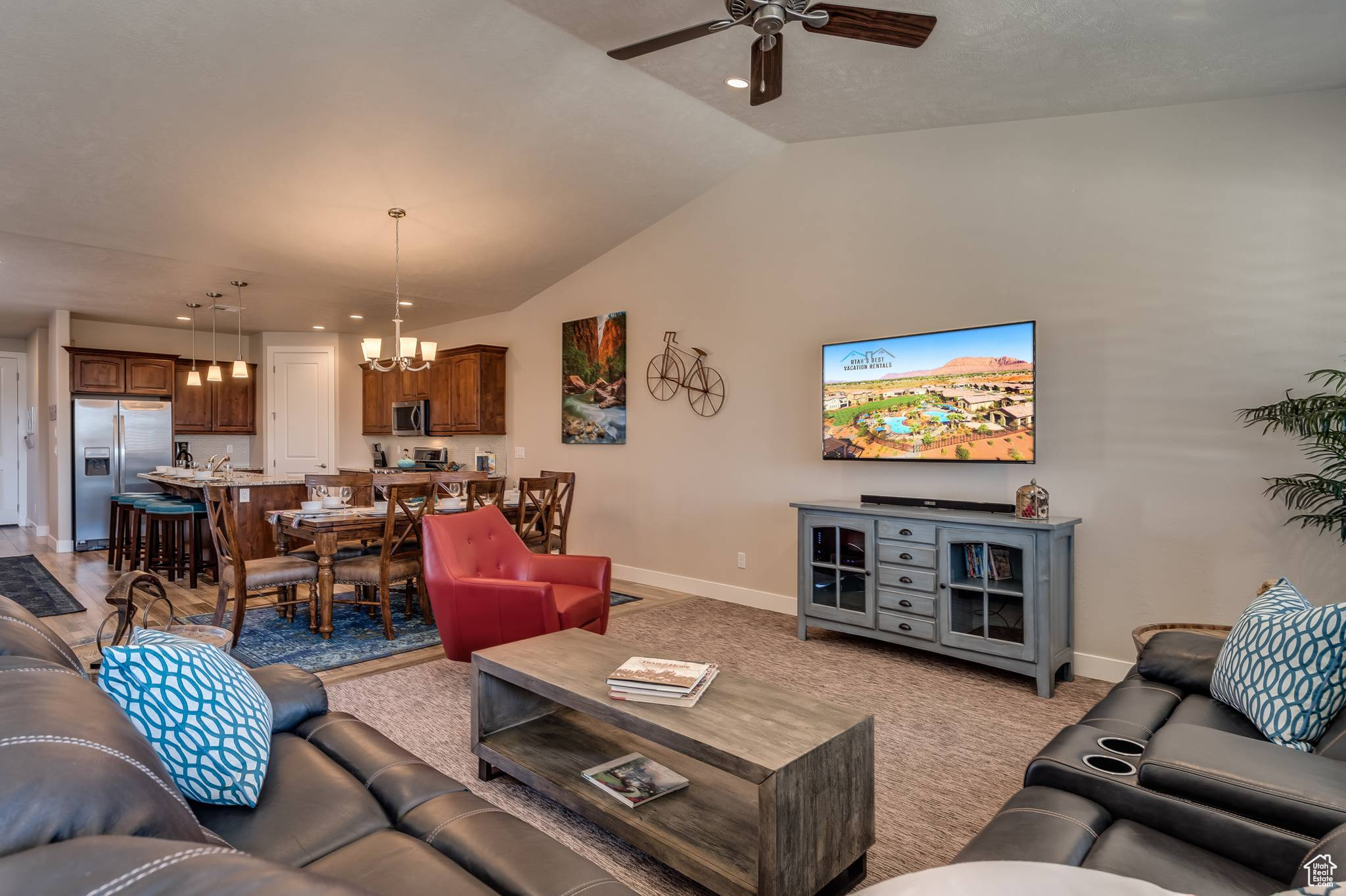 Carpeted living room featuring vaulted ceiling and ceiling fan with notable chandelier