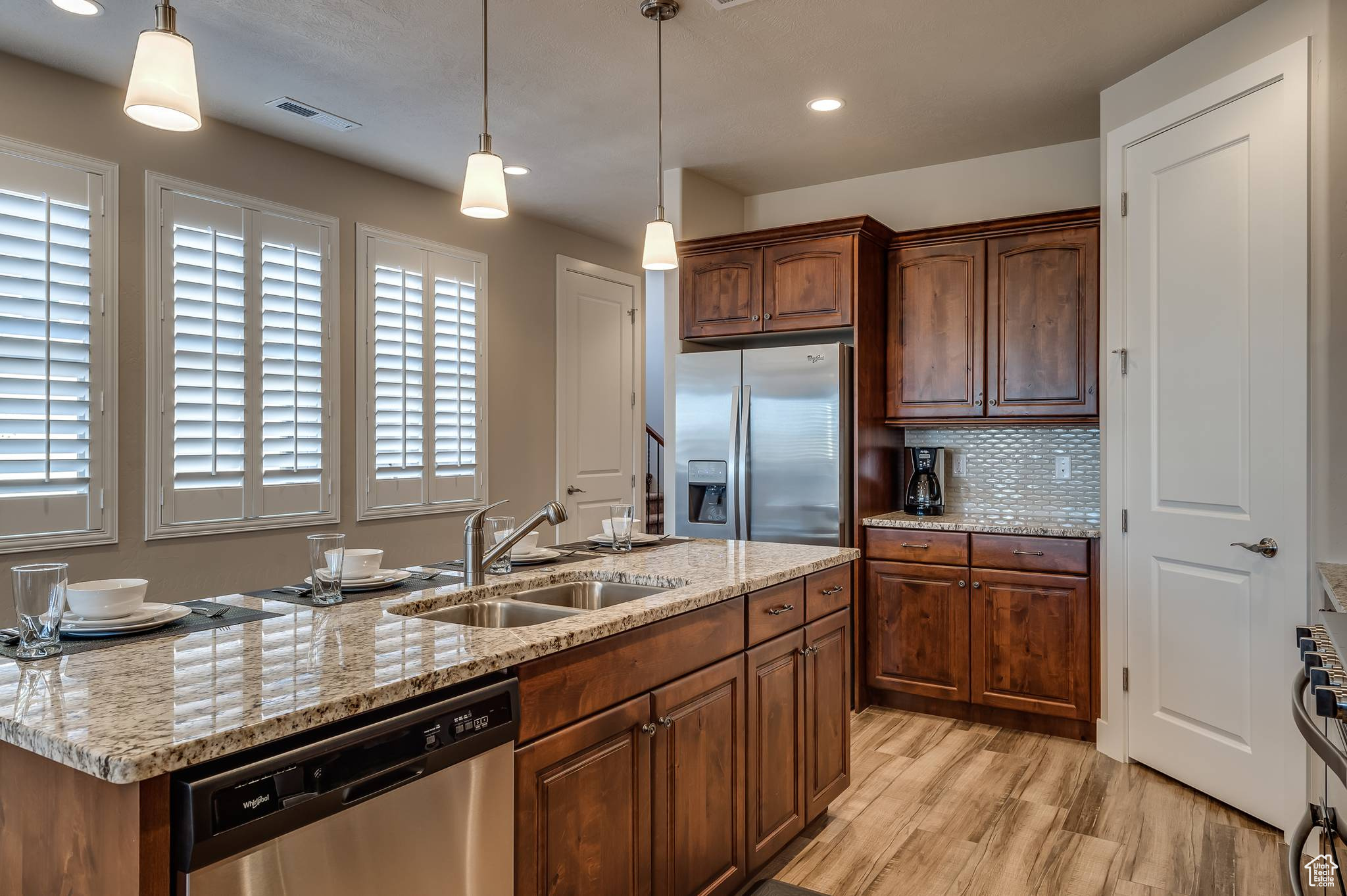 Kitchen with light hardwood / wood-style flooring, stainless steel appliances, a kitchen island with sink, backsplash, and sink