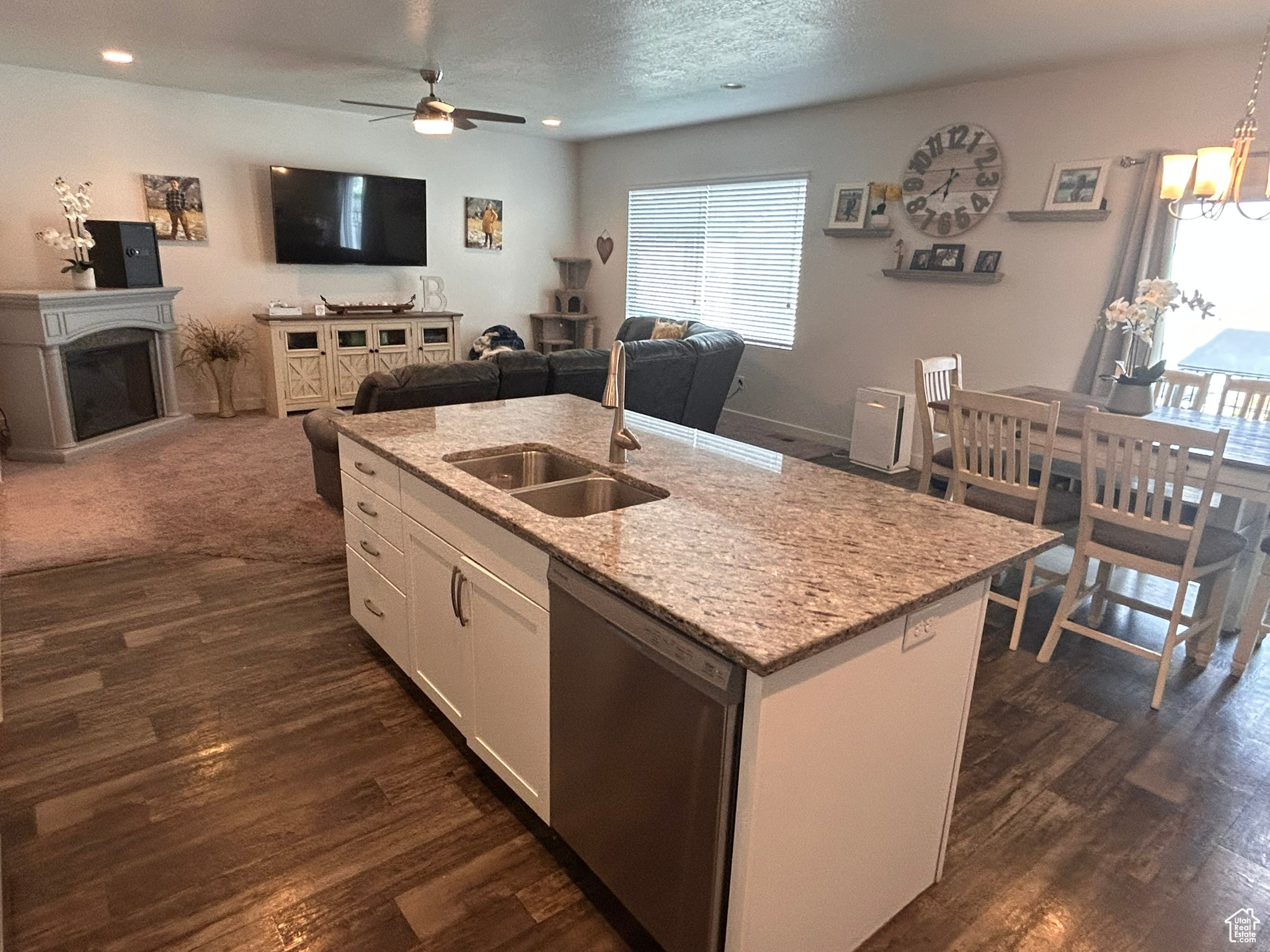 Kitchen with white cabinets, dark wood-type flooring, dishwasher, and a center island with sink