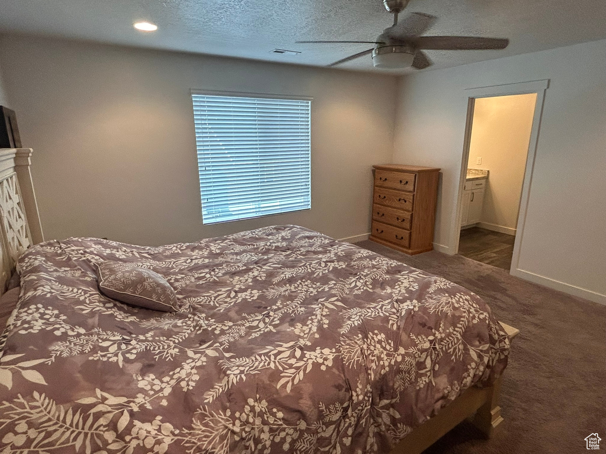 Carpeted bedroom featuring a textured ceiling, ceiling fan, and ensuite bath