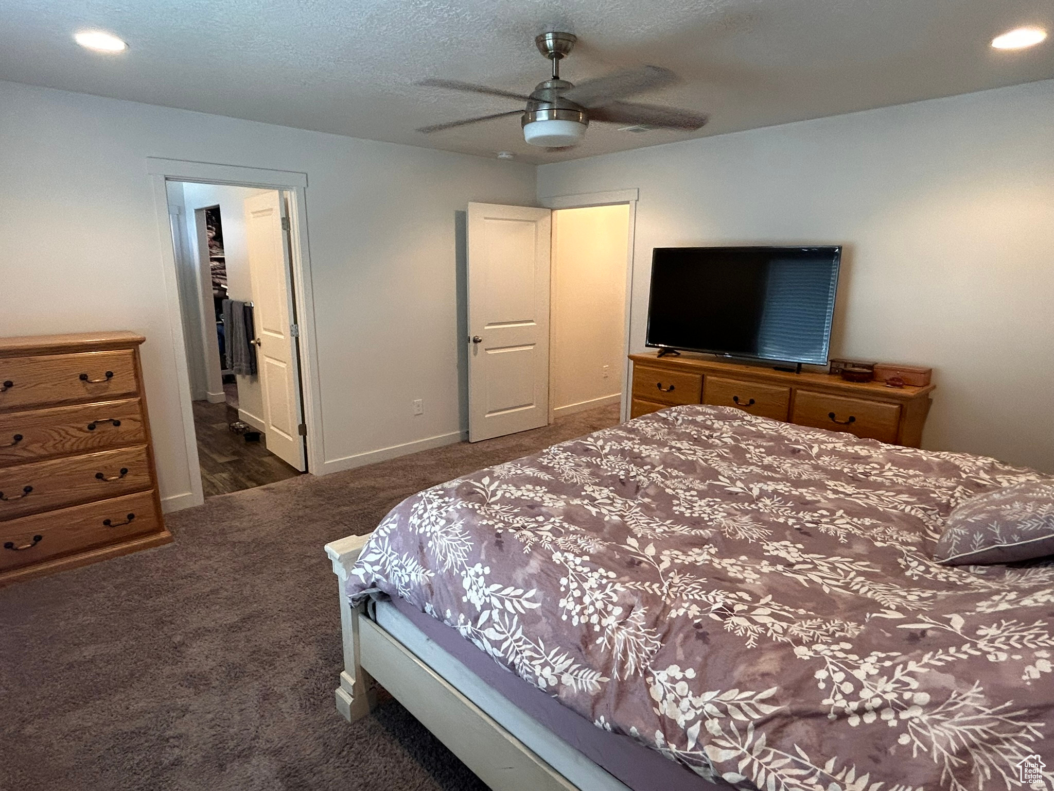 Carpeted bedroom with a textured ceiling, a closet, ceiling fan, and ensuite bath