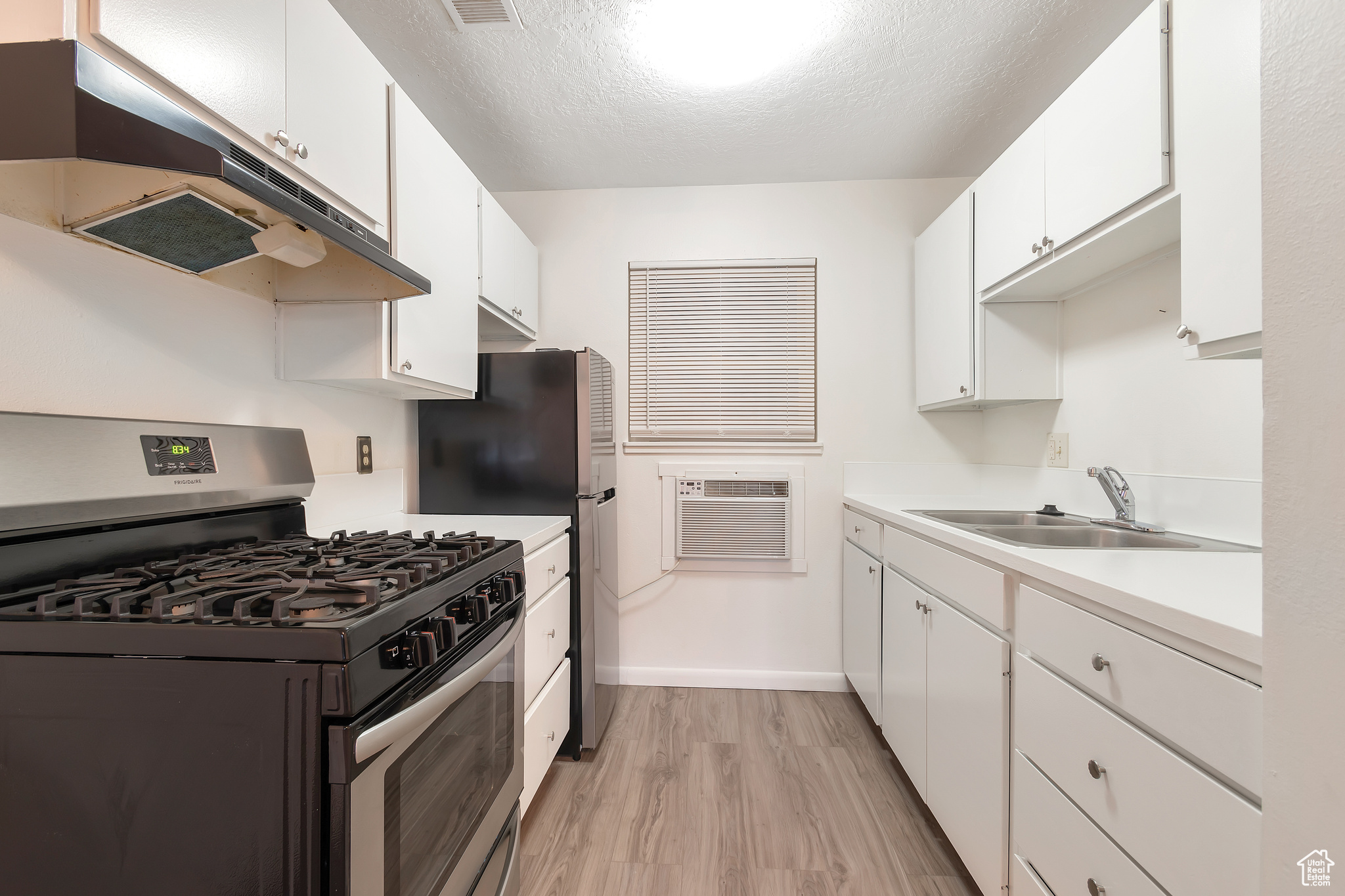 Kitchen with sink, light hardwood / wood-style flooring, gas range, and white cabinetry