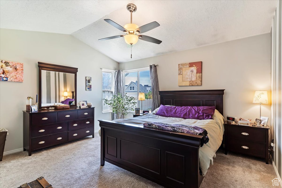 Bedroom with a textured ceiling, lofted ceiling, ceiling fan, and light colored carpet