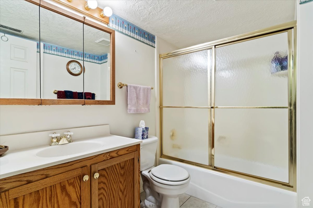 Full bathroom with tile flooring, a textured ceiling, combined bath / shower with glass door, vanity, and toilet