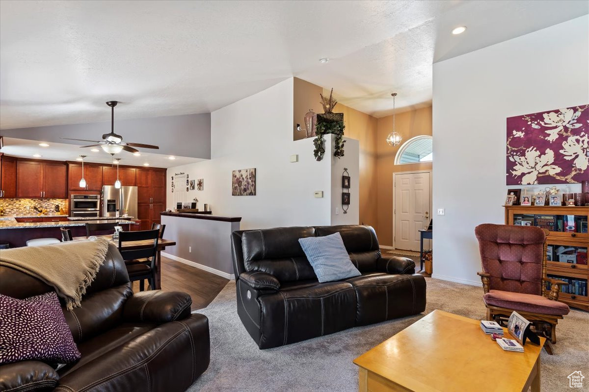 Carpeted living room with high vaulted ceiling and ceiling fan with notable chandelier