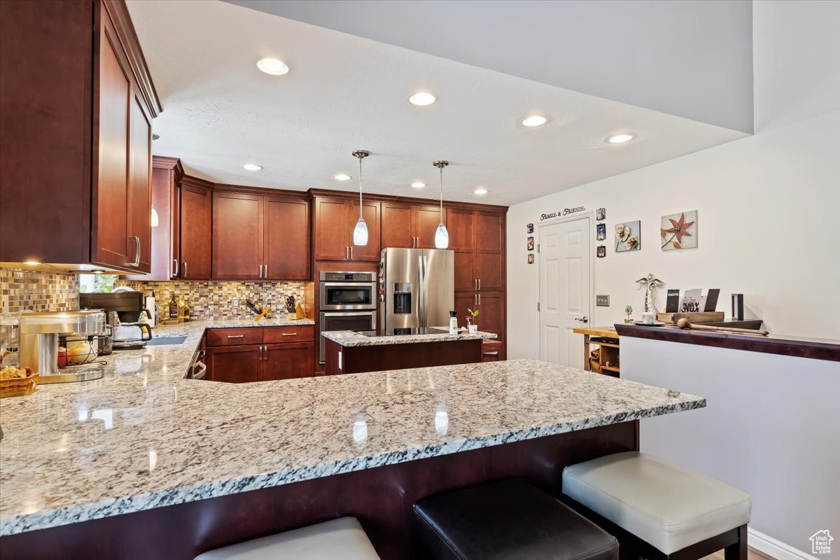 Kitchen with light stone countertops, stainless steel appliances, kitchen peninsula, pendant lighting, and tasteful backsplash