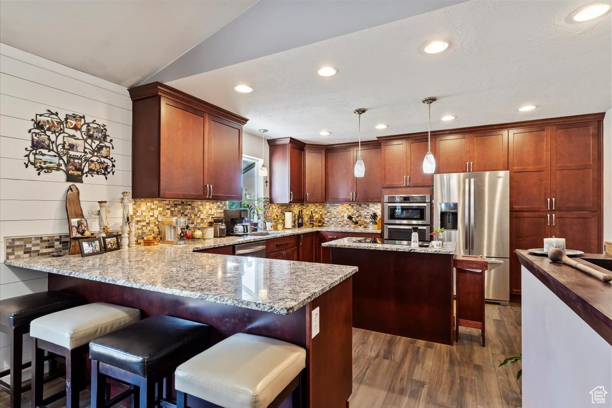 Kitchen with a center island, stainless steel appliances, light stone counters, and pendant lighting