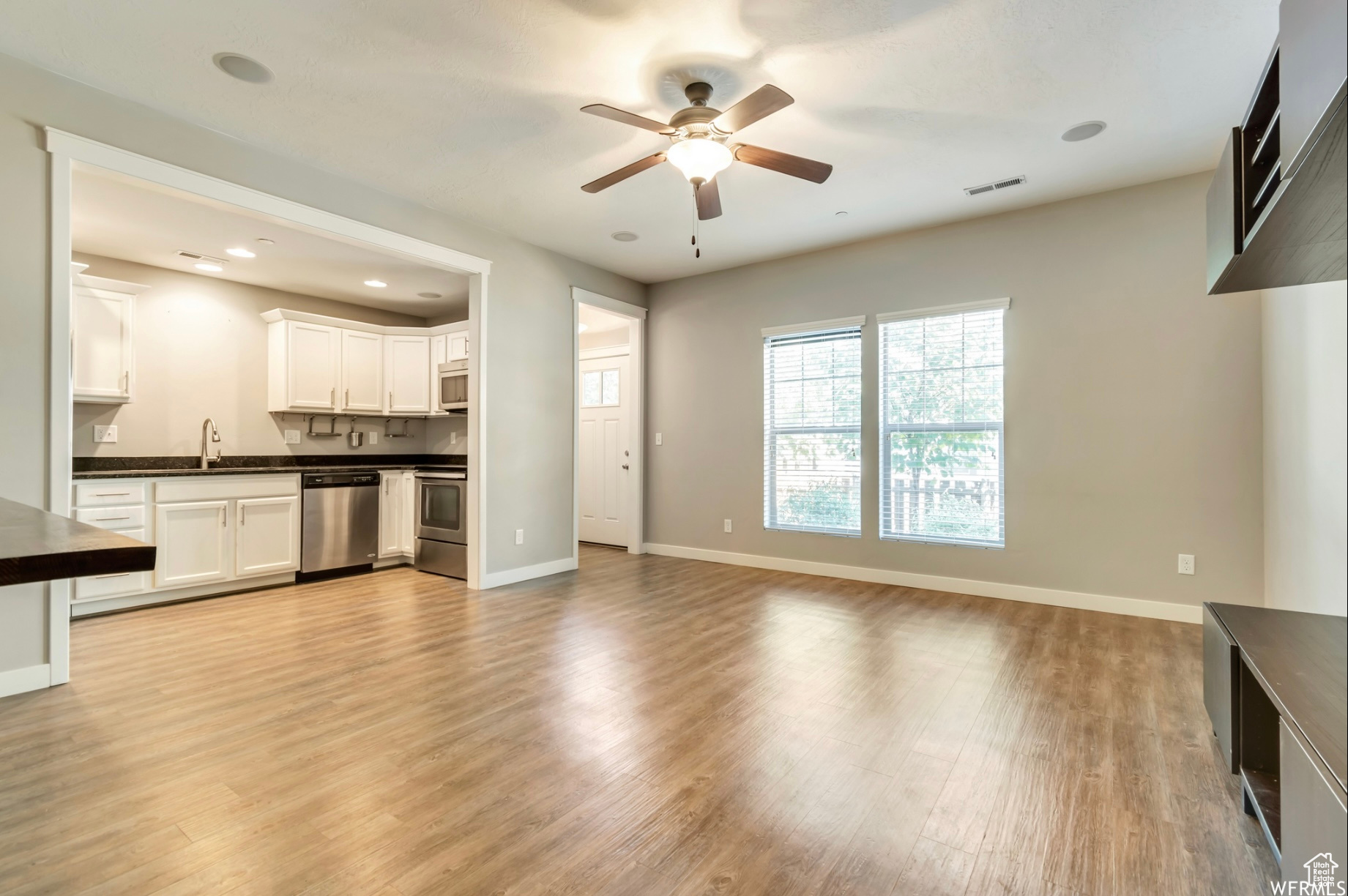 Unfurnished living room with ceiling fan, light wood-type flooring, and sink