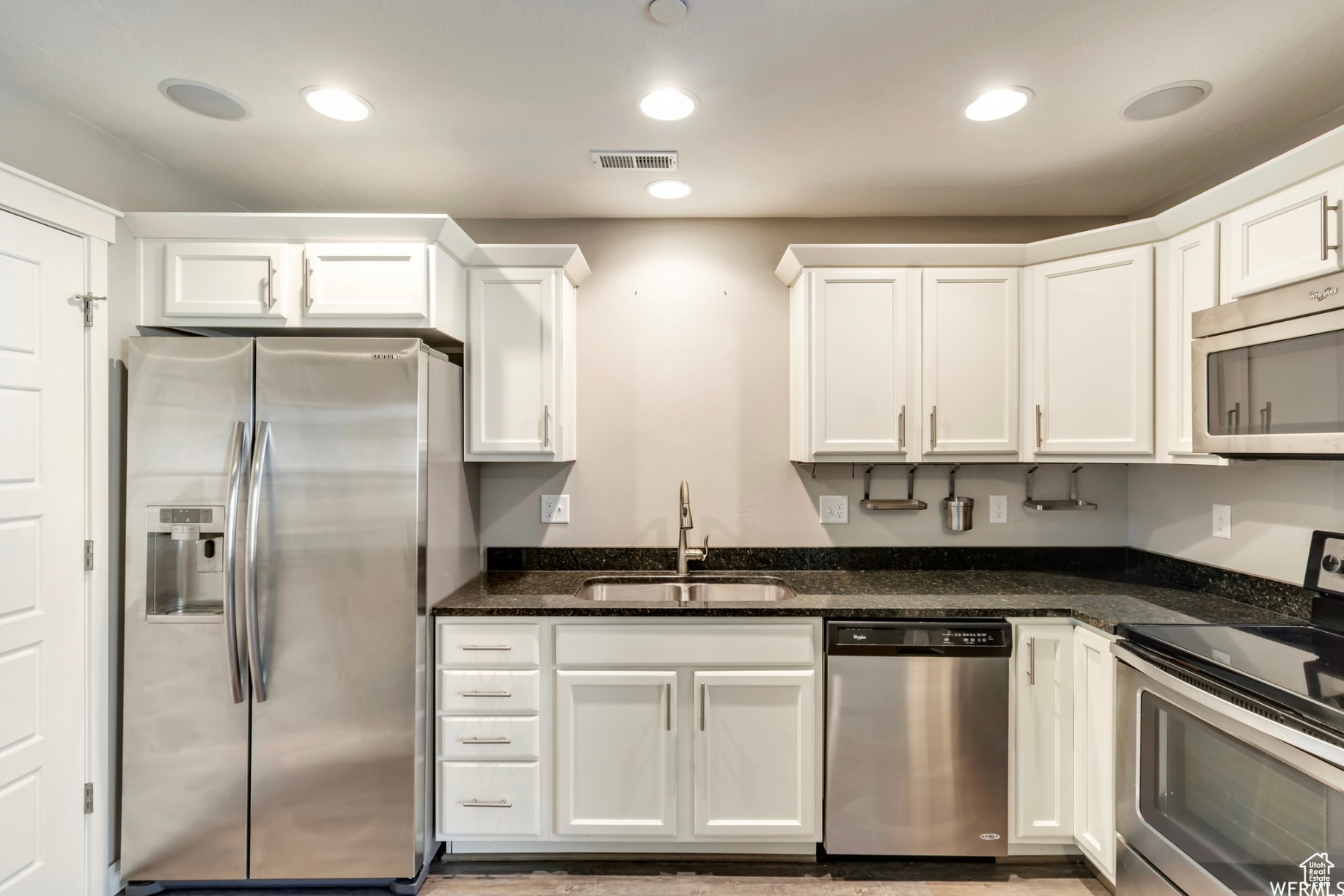 Kitchen featuring dark stone countertops, sink, white cabinets, and appliances with stainless steel finishes