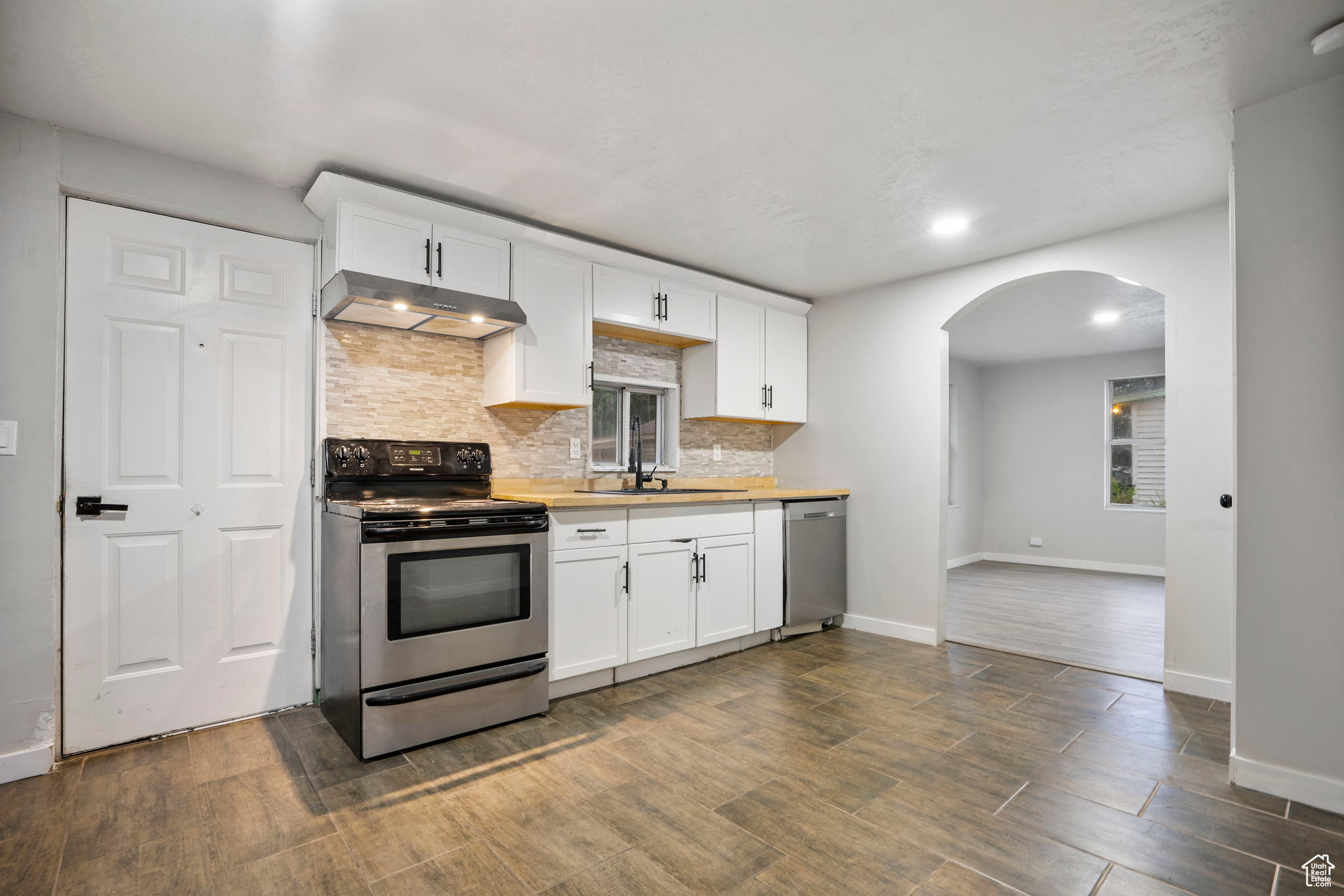 Kitchen featuring stainless steel appliances, white cabinets, wood-type flooring, sink, and tasteful backsplash