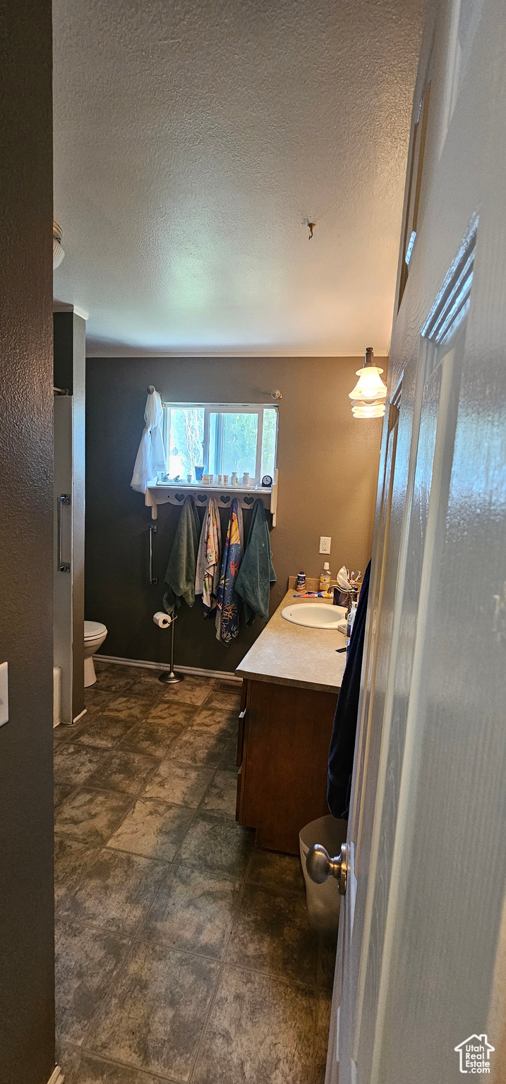 Bathroom with a textured ceiling, vanity, toilet, and tile floors