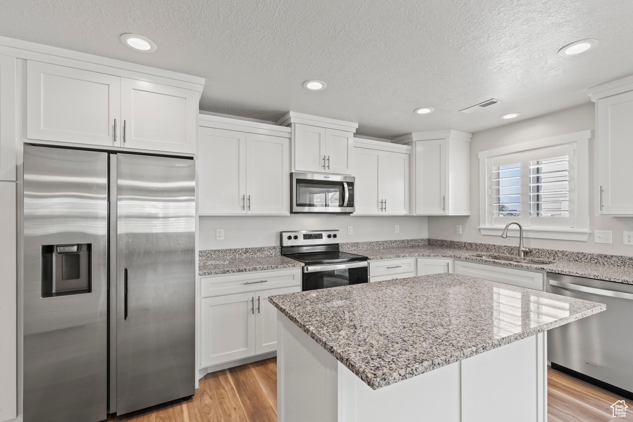 Kitchen with light wood-type flooring, stainless steel appliances, a center island, sink, and white cabinets