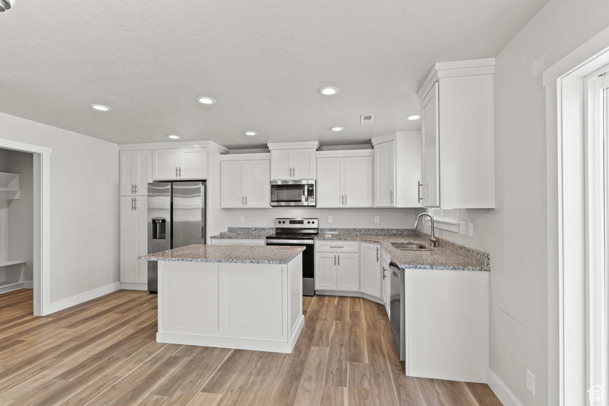 Kitchen featuring light wood-type flooring, appliances with stainless steel finishes, a kitchen island, and light stone countertops