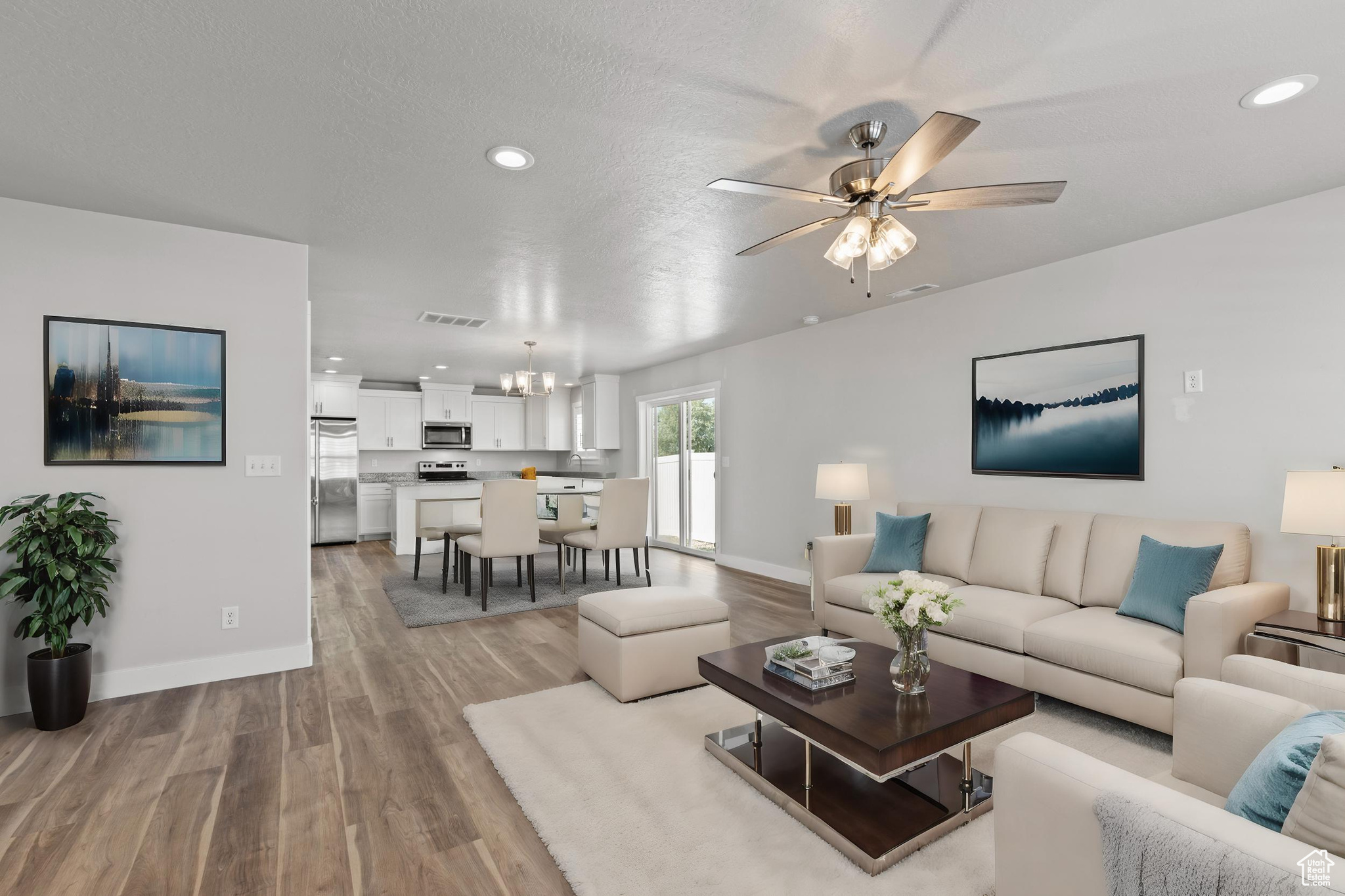 Living room featuring ceiling fan with notable chandelier, light hardwood / wood-style floors, and a textured ceiling AI generated