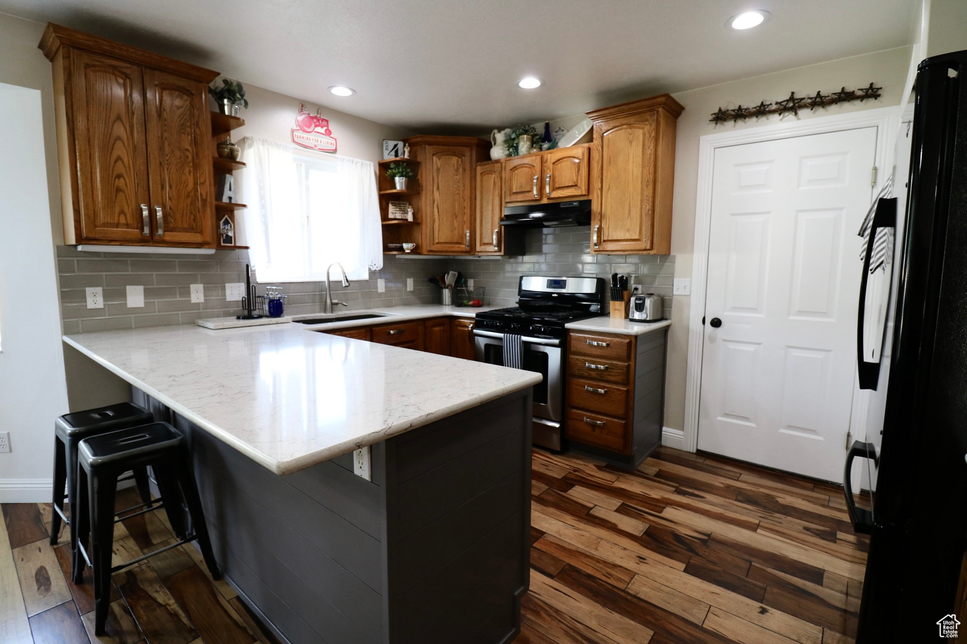 Kitchen featuring stainless steel gas range oven, dark hardwood / wood-style floors, backsplash, black refrigerator, and sink